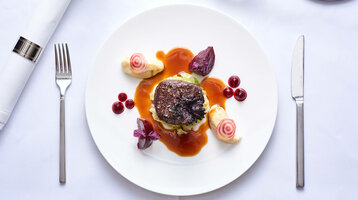 Gourmetgericht auf weißem Teller mit Fleisch, Soße, Gemüse und dekorativen Beilagen, stilvoll angerichtet.