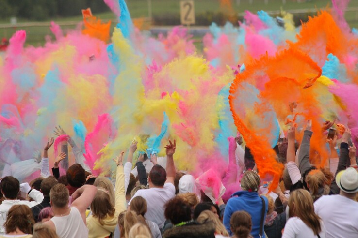 Menschen werfen bunte Farbpulver in die Luft bei einem Fest auf der Galopprennbahn in Bremen.