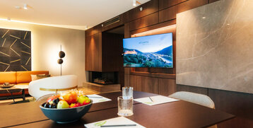 Moderner Meetingraum im ATLANTIC Hotel Heidelberg mit Holzdekor, TV, Sofa und Tisch mit Obstschale.