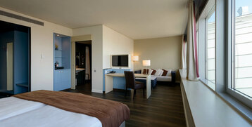 Modern hotel room with double bed, sitting area, desk, large window and view of the bathroom at the ATLANTIC Hotel Sail City.