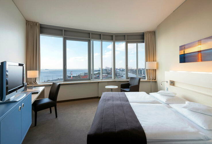 Helles Hotelzimmer mit Doppelbett, großem Fenster und Blick auf den Hafen von Bremerhaven.