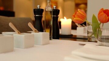Eleganter Tisch mit Kerze, Tulpen, Ölflasche und Gewürzmühlen, ideal für ein stilvolles Dinner im Hotelrestaurant.