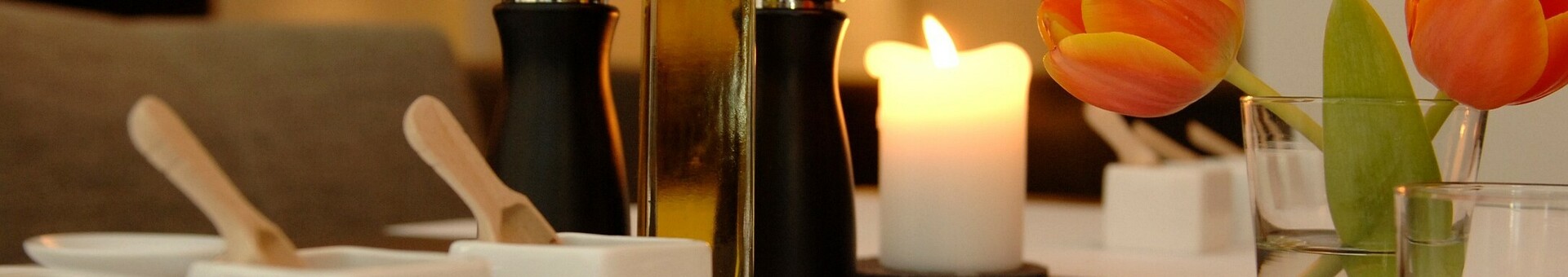 Eleganter Tisch mit Kerze, Tulpen, Ölflasche und Gewürzmühlen, ideal für ein stilvolles Dinner im Hotelrestaurant.