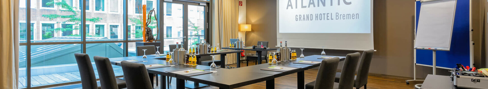 Moderner Konferenzraum im ATLANTIC Grand Hotel Bremen mit U-förmiger Bestuhlung, Präsentationsleinwand und Flipchart.