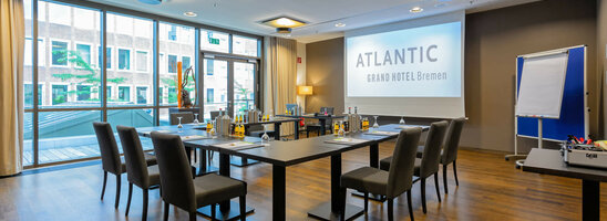 Moderner Konferenzraum im ATLANTIC Grand Hotel Bremen mit U-förmiger Bestuhlung, Präsentationsleinwand und Flipchart.