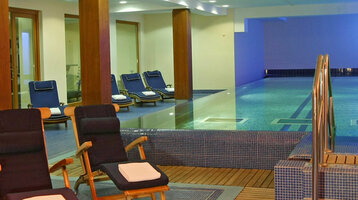 Modernes Hallenbad mit Liegestühlen und stimmungsvoller Beleuchtung im ATLANTIC Grand Hotel Travemünde.