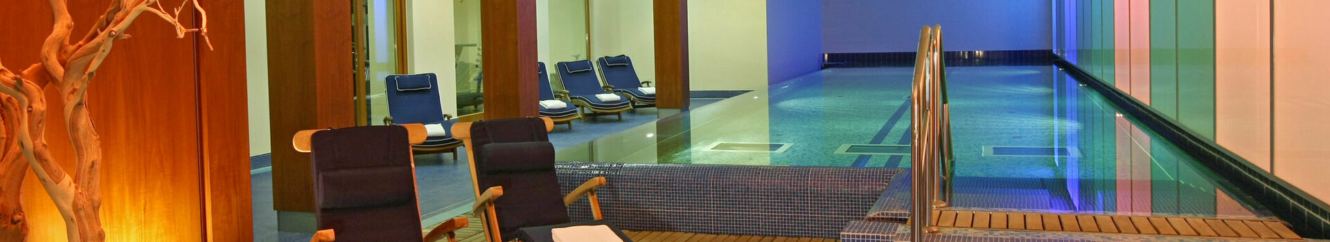 Modernes Hallenbad mit Liegestühlen und stimmungsvoller Beleuchtung im ATLANTIC Grand Hotel Travemünde.