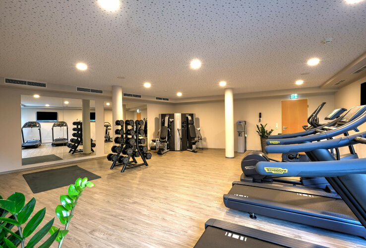 Bright fitness room at the ATLANTIC Hotel Bremen with treadmills, dumbbells and training equipment on a wooden floor.