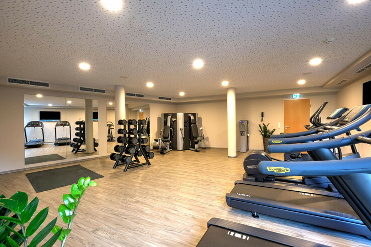 Bright fitness room at the ATLANTIC Hotel Bremen with treadmills, dumbbells and training equipment on a wooden floor.