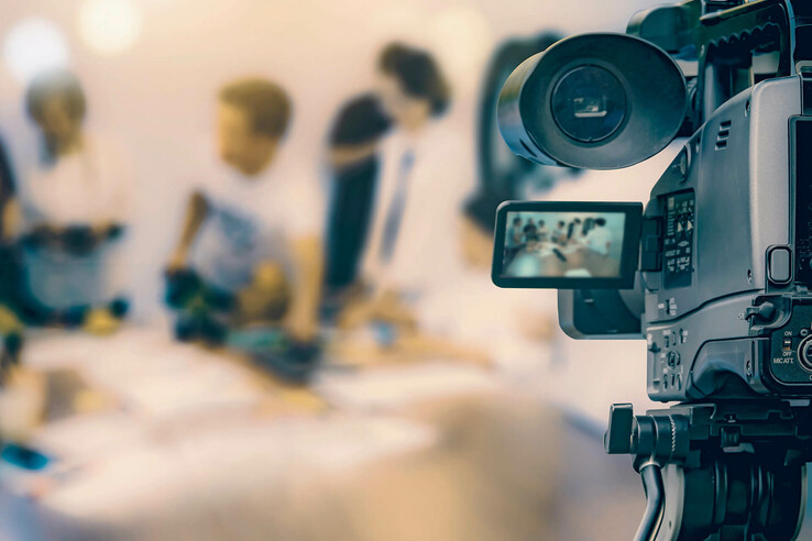 Eine Kamera filmt eine unscharfe Szene mit mehreren Personen im Hintergrund.