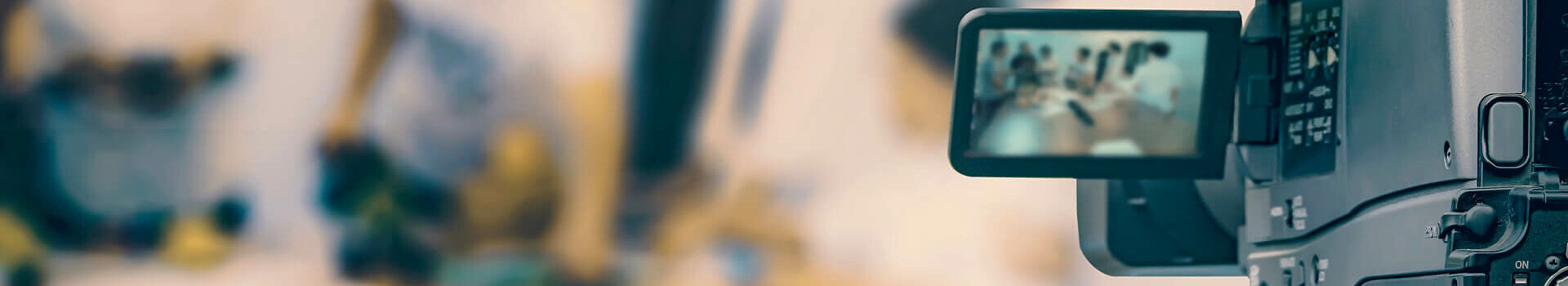 Eine Kamera filmt eine unscharfe Szene mit mehreren Personen im Hintergrund.