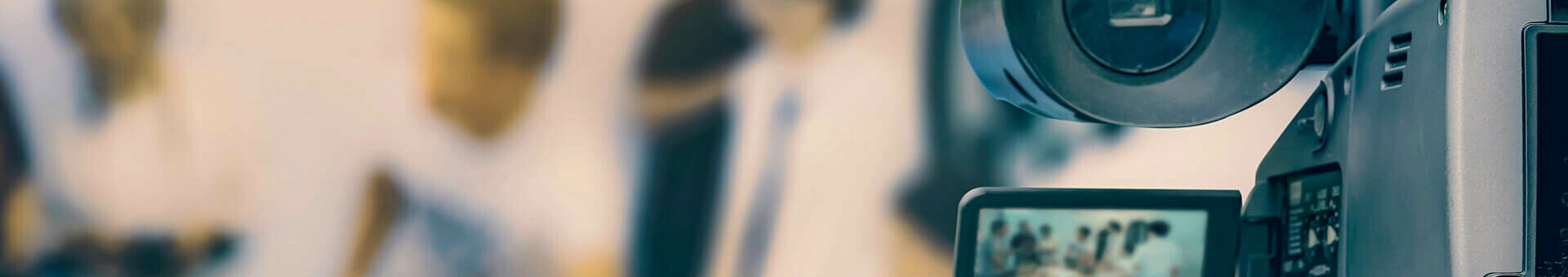 Eine Kamera filmt eine unscharfe Szene mit mehreren Personen im Hintergrund.