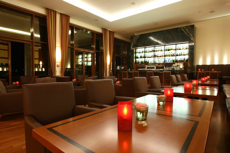 Elegante Hotelbar mit gemütlichen Sesseln, Holztischen, roten Kerzen und beleuchteter Rückwand mit Spirituosen.
