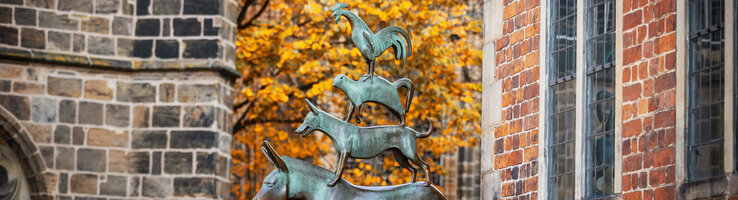 Bronze statue of the Bremen Town Musicians in front of an autumnal tree and brick building.