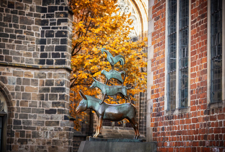 Bronze statue of the Bremen Town Musicians in front of an autumnal tree and brick building.