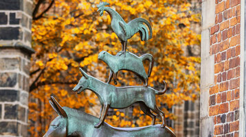 Bronzestatue der Bremer Stadtmusikanten vor herbstlichem Baum und Backsteingebäude.