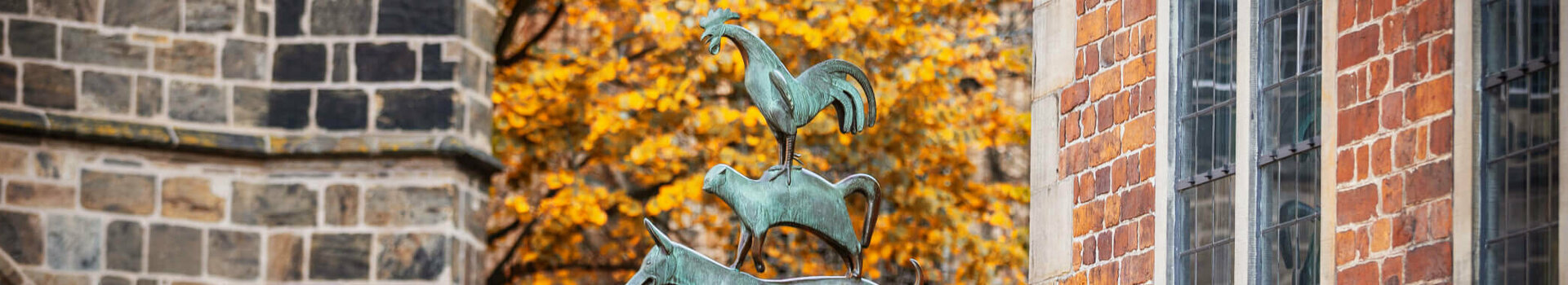ATLANTIC Grand Hotel Bremen Goldener Herbst Stadtmusikanten Bronzestatue der Bremer Stadtmusikanten vor herbstlichem Baum und Backsteingebäude.