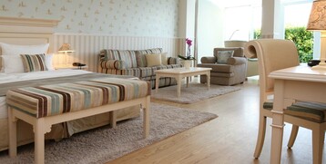 Bright hotel room with double bed, cozy sitting area, desk and large windows with a view of the greenery.