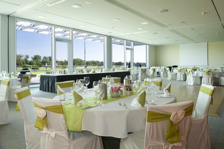 Die passende Räumlichkeit für Ihren Geburtstag oder eine romantische Hochzeitfeier in Bremen Eleganter Festsaal im ATLANTIC Hotel Galopprennbahn, mit gedeckten Tischen und Blick auf die grüne Rennbahn.