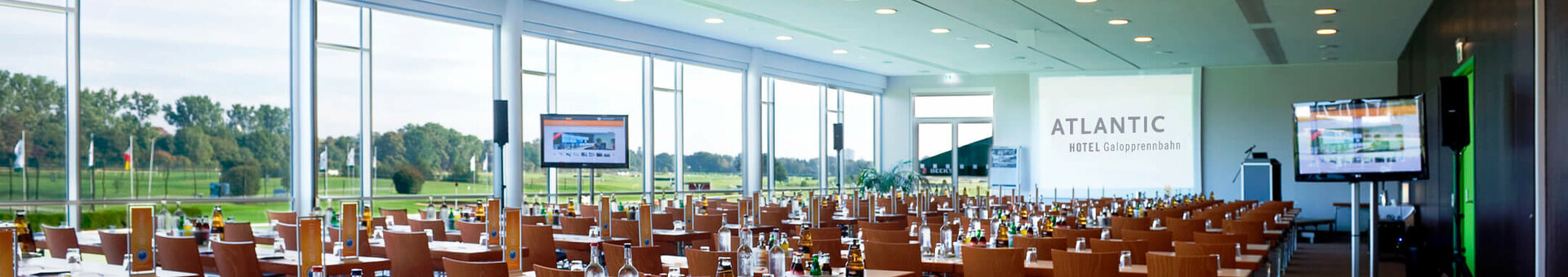 Large, bright conference room in the ATLANTIC Hotel Galopprennbahn with tables, chairs and a view of the racecourse.