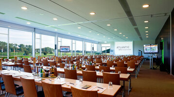 Function rooms St. Andrews and Augusta with a view onto green Large, bright conference room in the ATLANTIC Hotel Galopprennbahn with tables, chairs and a view of the racecourse.
