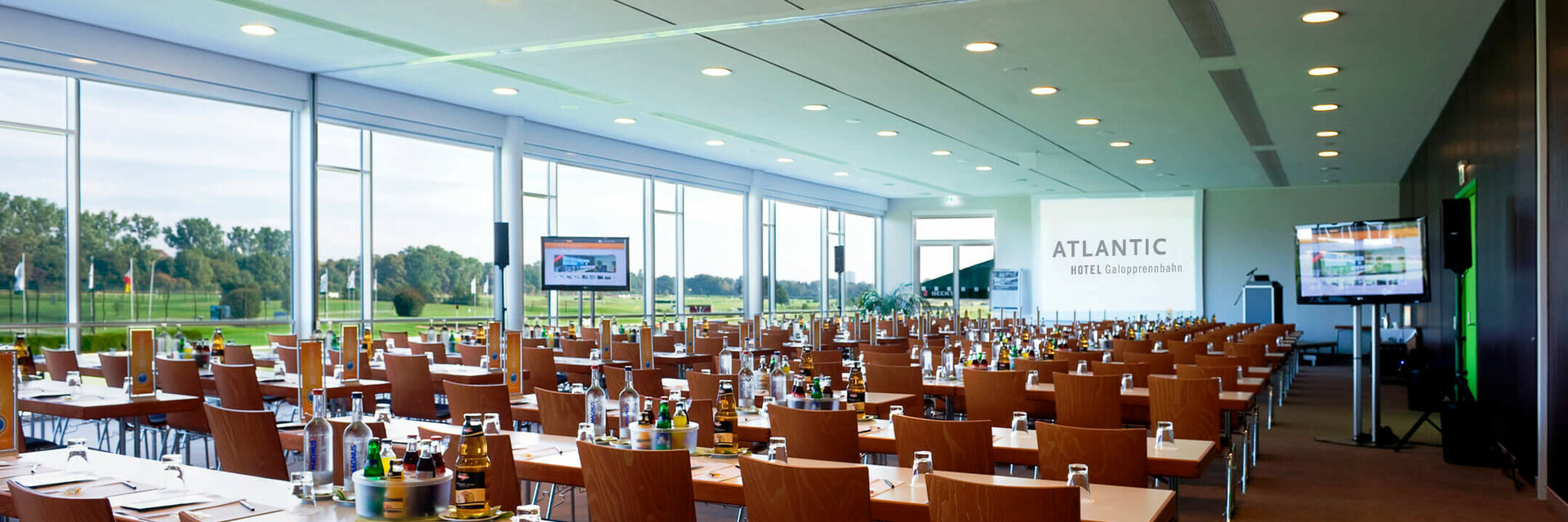 Großer, heller Konferenzraum im ATLANTIC Hotel Galopprennbahn mit Tischen, Stühlen und Blick auf die Rennbahn.