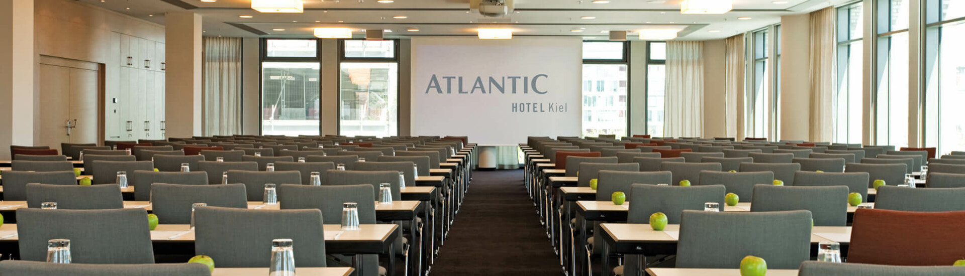Modern conference room in the ATLANTIC Hotel Kiel with rows of gray chairs, tables, glasses and green apples.