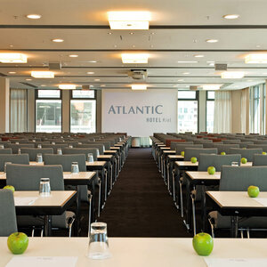 Moderner Konferenzraum im ATLANTIC Hotel Kiel mit Reihen grauer Stühle, Tischen, Gläsern und grünen Äpfeln.