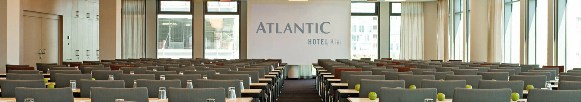Moderner Konferenzraum im ATLANTIC Hotel Kiel mit Reihen grauer Stühle, Tischen, Gläsern und grünen Äpfeln.