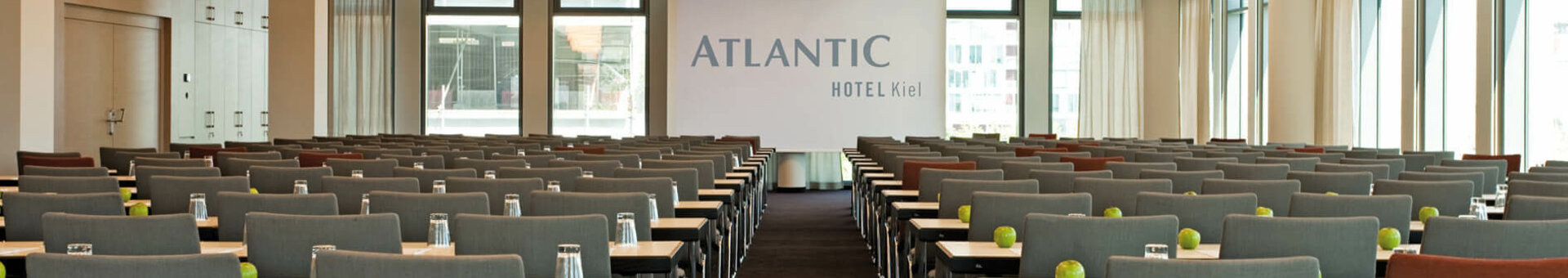 Moderner Konferenzraum im ATLANTIC Hotel Kiel mit Reihen grauer Stühle, Tischen, Gläsern und grünen Äpfeln.