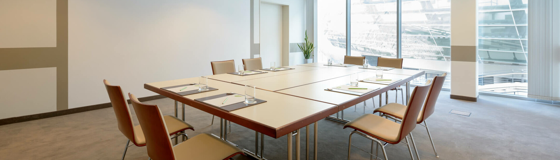 Tagungsraum Conference Saal 3 des ATLANTIC Hotel Sail City in Blockbestuhlung Moderner Konferenzraum mit großem Tisch, acht Stühlen und Panoramafenster im ATLANTIC Hotel Sail City Bremerhaven.