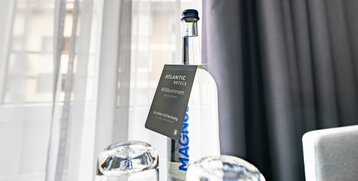 Wasserflasche mit Willkommensschild und Gläsern auf einem Tisch im ATLANTIC Hotel Vegesack, Bremen.