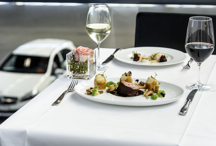Elegantes Abendessen mit Fleischgericht, Rot- und Weißwein auf weiß gedecktem Tisch, dekoriert mit einer rosa Blume.