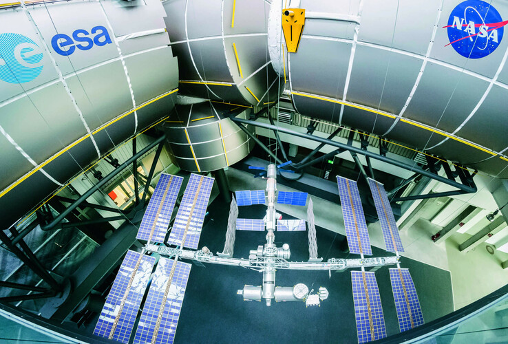 Model of the International Space Station with solar panels, surrounded by large metal structures with ESA and NASA logos.