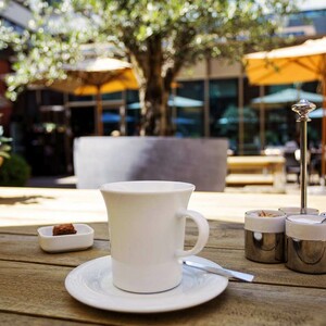 Cup of coffee on a wooden table in the sunny hotel garden with parasols and plants at the ATLANTIC Grand Hotel Bremen.