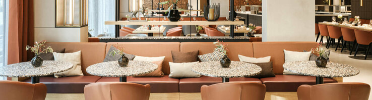 Modernes Restaurant im ATLANTIC Hotel Münster mit stilvollen Tischen, bequemen Sesseln und dekorativen Pflanzen.