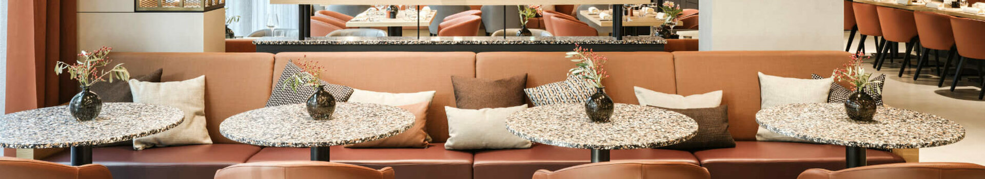 Modernes Restaurant im ATLANTIC Hotel Münster mit stilvollen Tischen, bequemen Sesseln und dekorativen Pflanzen.