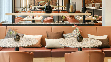 Modernes Restaurant im ATLANTIC Hotel Münster mit stilvollen Tischen, bequemen Sesseln und dekorativen Pflanzen.