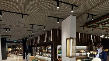 Moderne Hotel-Lobby mit Empfangstresen, beleuchtetem Regal und Mitarbeiterin mit Maske.