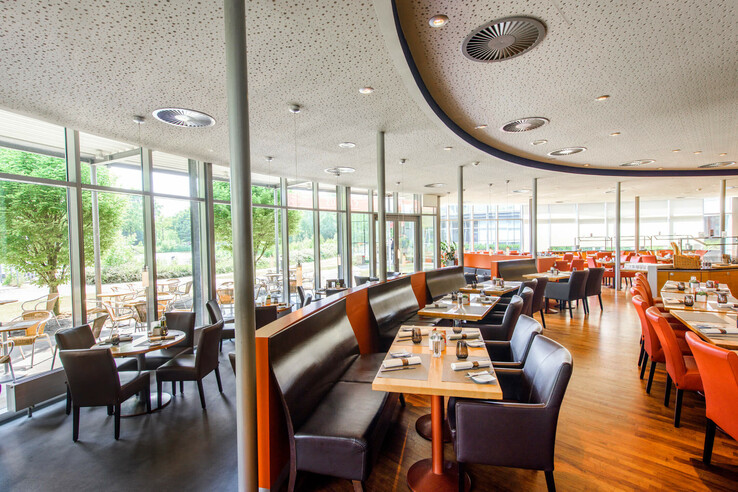 Helles Hotelrestaurant mit großen Fenstern, modernem Interieur, braunen und orangefarbenen Stühlen, Blick ins Grüne.