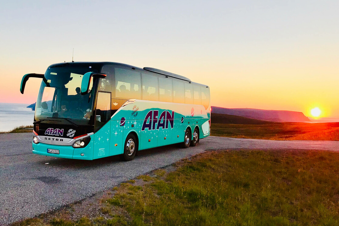 A coach at sunset on a hill with a sea view in the background.