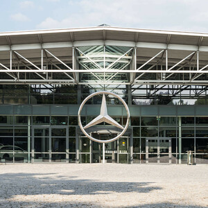 Moderne Glasfassade mit großem, silbernem Mercedes-Stern über dem Eingang.