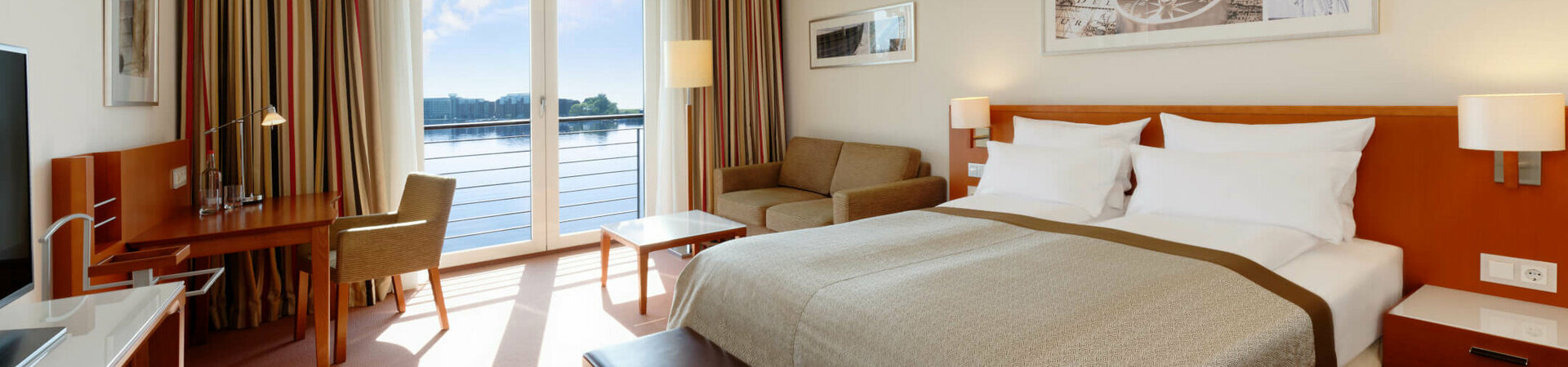 Superior Room with a view over the harbour in the ATLANTIC Hotel Wilhelmshaven  Bright hotel room with double bed, sofa, desk and large window with lake view.