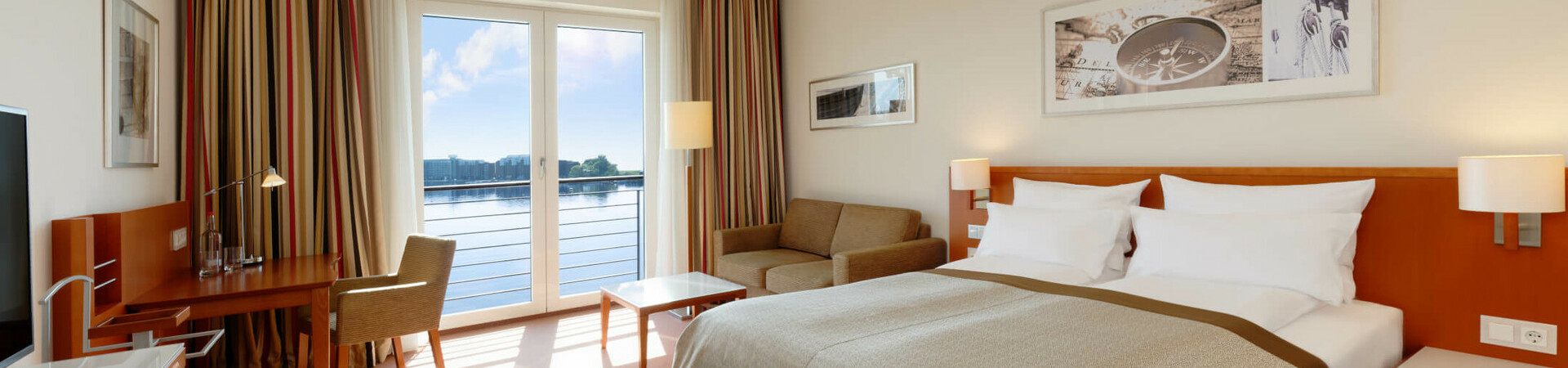 Superior Zimmer mit Blick auf den Hafen im ATLANTIC Hotel Wilhelmshaven Helles Hotelzimmer mit Doppelbett, Sofa, Schreibtisch und großem Fenster mit Seeblick.