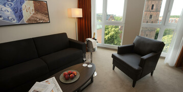 Modern hotel room with sofa, armchair, table, champagne and a view of Bremen's church tower through large windows.