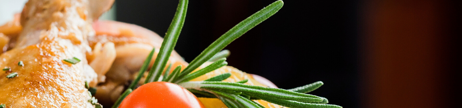 Close-up of a roasted chicken with rosemary and cherry tomatoes, served at the ATLANTIC Hotel Galopprennbahn.
