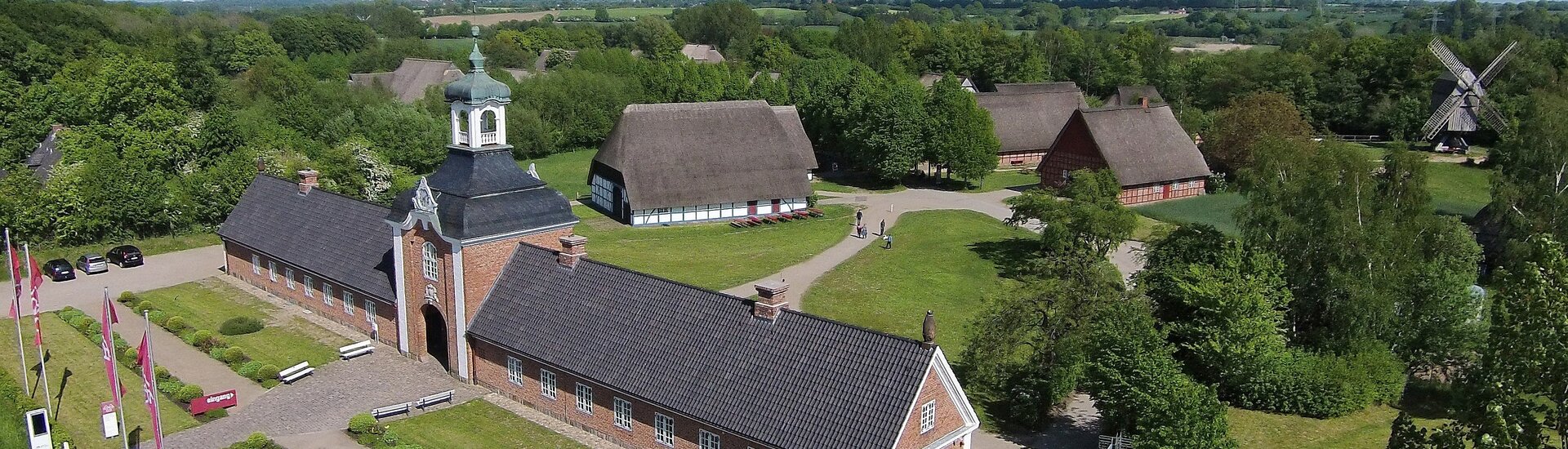 Terrain of the outdoor museum Wolfsee photographed for a bird's eye view Historic brick building with tower, surrounded by green countryside and traditional thatched roof houses.