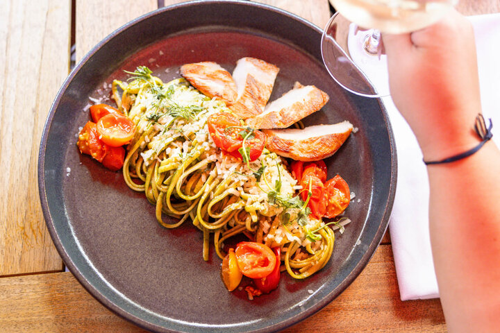 Dining at the ATLANTIC Hotel Landgut Horn Bremen Plate with pasta, grilled chicken, cherry tomatoes and herbs, hand holding a glass of wine.