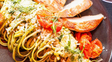 Teller mit Pasta, gegrilltem Hähnchen, Kirschtomaten und Kräutern, Hand hält ein Glas Wein.