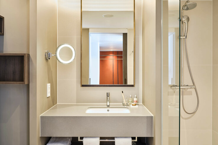 Modern hotel bathroom with washbasin, illuminated mirror and rain shower at the ATLANTIC Hotel Münster.